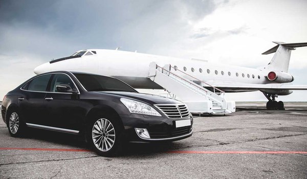 A black luxury car of shuttle service in front of a white charter airplane parked at Austin airport.